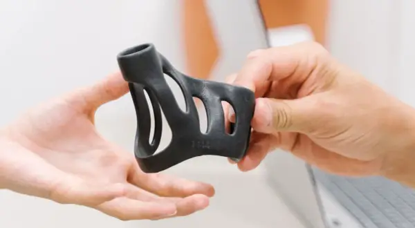 Eine Hand reicht eine schwarze Schiene, die zur Behandlung eines Schnappfingers dient, einer anderen Hand.