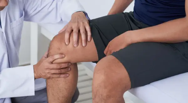 Arzt untersucht Knie eines Mannes, der über Schmerzen beim Knien auf hartem Boden klagt.