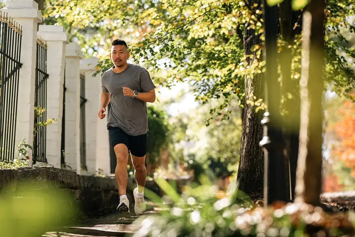 Ein Mann in Sportkleidung geht laufen, die Sonne scheint durch die Bäume.