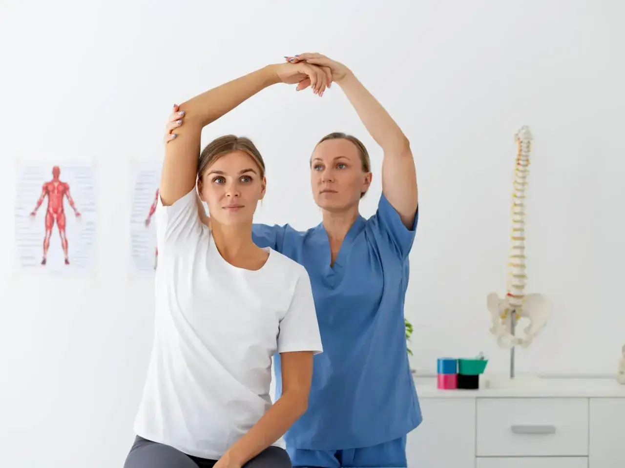 Physiotherapie: Eine Patientin hebt den Arm, während eine Therapeutin sie unterstützt. Im Hintergrund ein Skelettmodell.