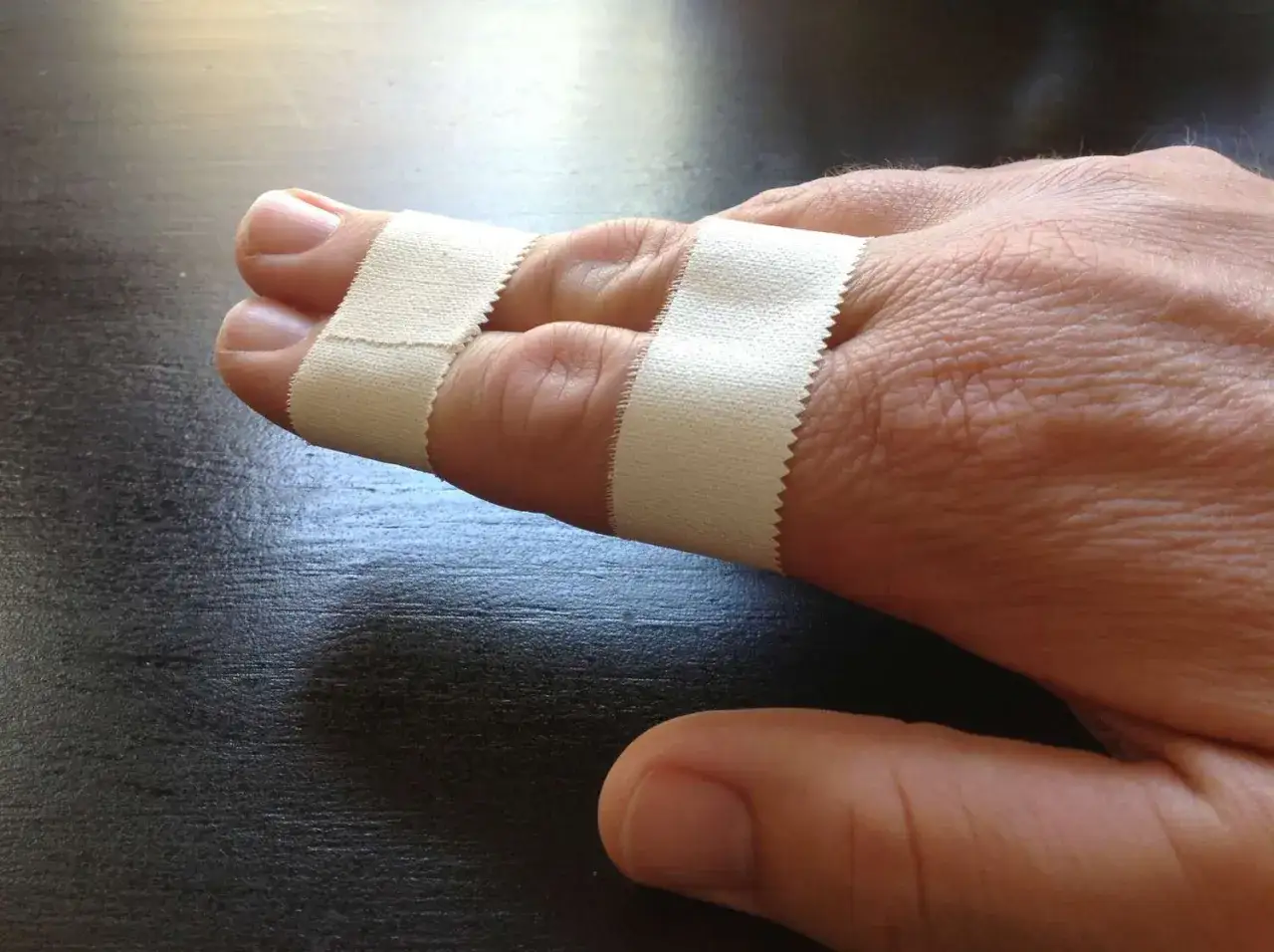 Zwei Finger sind mit Tape verbunden, um sie zu stabilisieren. Das Finger tapen hilft bei der Heilung.