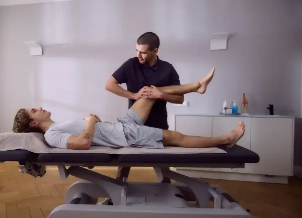 Physiotherapeut führt krankengymnastik hws durch, indem er das Bein eines liegenden Patienten sanft bewegt.